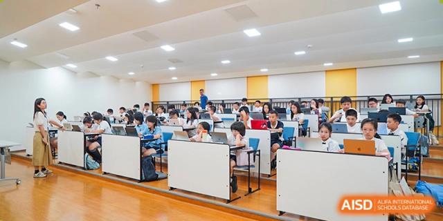 A large classroom filled with students at Shenzhen Foreign Languages GBA Academy working on laptops and assignments at their desks.