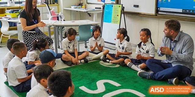 Young students at Shenzhen Foreign Languages GBA Academy sitting on a green rug and collaborating on a project.