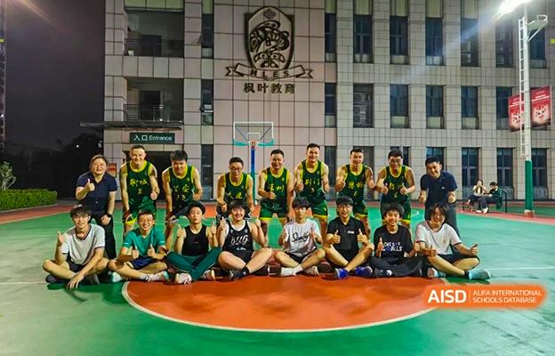 The Shenzhen Foreign Languages GBA Academy basketball team sitting on the court after a game, posing for a group photo.