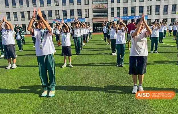 Students at Shenzhen Foreign Languages GBA Academy participating in a group exercise or activity on a grassy sports field.