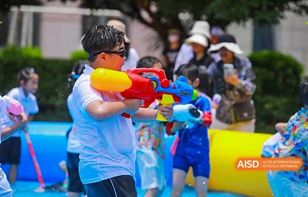 A student at Shenzhen Foreign Languages GBA Academy smiling and holding a water gun while standing in an inflatable pool.