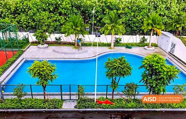 An outdoor swimming pool surrounded by a manicured lawn and palm trees at Shenzhen Foreign Languages GBA Academy.