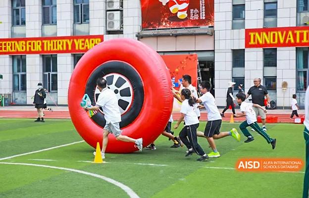 Students at Shenzhen Foreign Languages GBA Academy running and jumping through a large, red inflatable ring during a school event.
