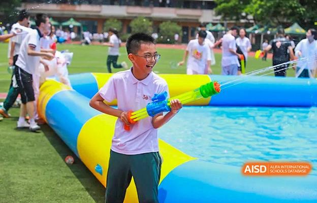 A male student at Shenzhen Foreign Languages GBA Academy laughing and holding a water gun while participating in a water activity.