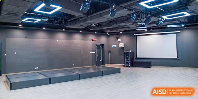 An empty black box theater or multipurpose room with a small stage and basketball hoop at Shenzhen Foreign Languages GBA Academy.