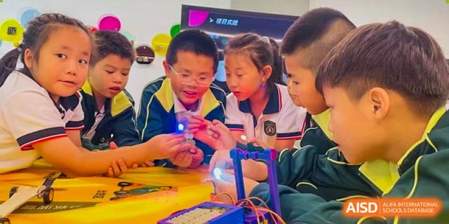 Two students from Maple Leaf International Academy Shenzhen are conducting a science experiment in a classroom, with one student holding a glowing light.