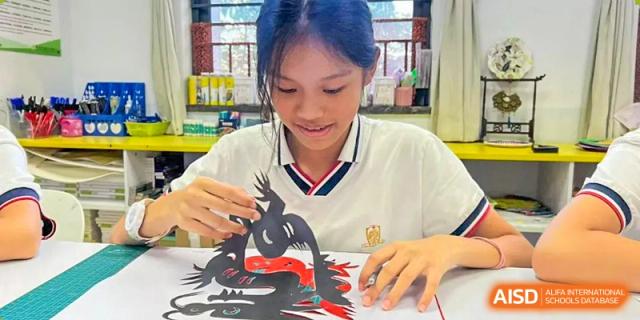 A female student from Maple Leaf International Academy Shenzhen is focused on cutting out a paper craft.