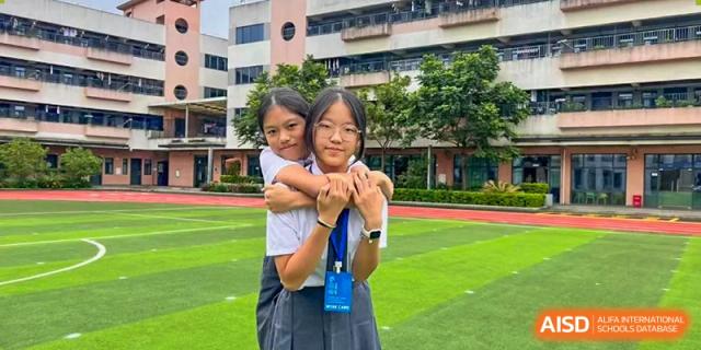 Two female students from Maple Leaf International Academy Shenzhen are smiling and hugging each other on a sports field.