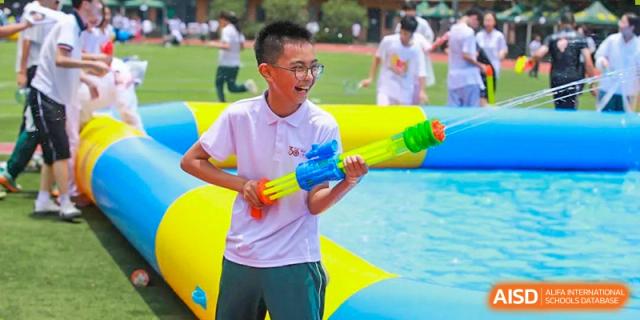 A male student from Maple Leaf International Academy Shenzhen is standing in a pool of water, holding a water gun and smiling at the camera.