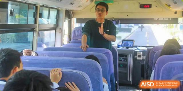 A teacher from Maple Leaf International Academy Shenzhen is standing in the aisle of a school bus, interacting with the students.