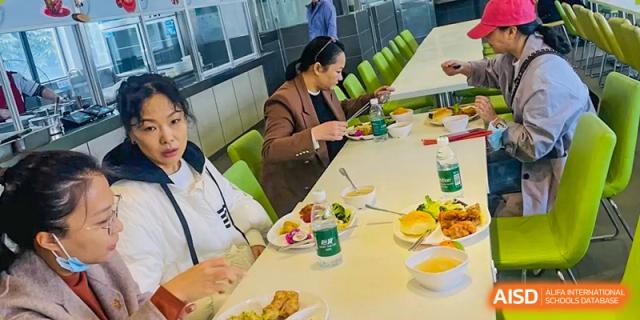 Two people from Maple Leaf International Academy Shenzhen are seated at a dining table, eating lunch.