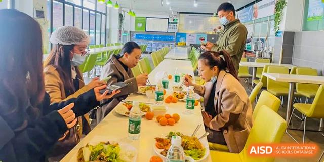 A group of people from Maple Leaf International Academy Shenzhen are eating lunch at a dining table with a variety of healthy food options.
