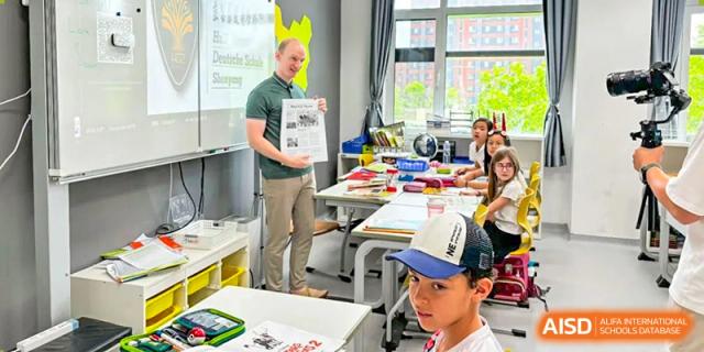 A teacher at HuZ Deutsche Schule Shenyang holding up a project for a student in a classroom setting.