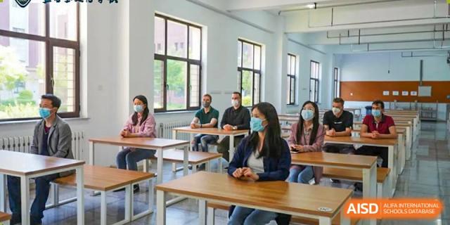 A group of adults and a student at HuZ Deutsche Schule Shenyang seated at desks in a classroom.