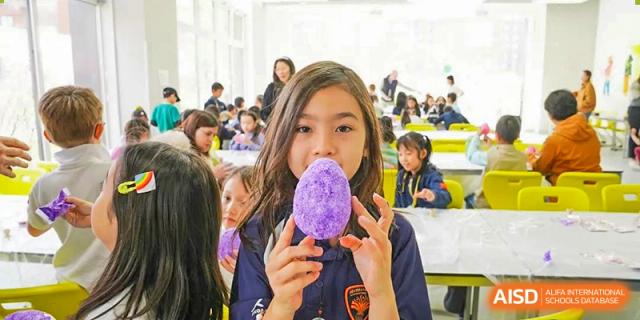 A female student at HuZ Deutsche Schule Shenyang holding up a purple, egg-shaped craft project.