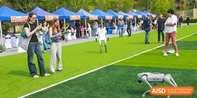 A robot at HuZ Deutsche Schule Shenyang walking across a green sports field with tents in the background.