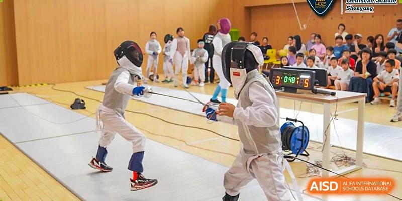 Two students wearing protective gear are fencing in a gym at HuZ Deutsche Schule Shenyang.