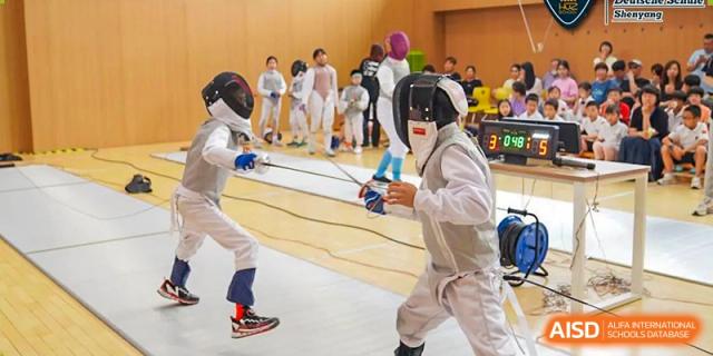 Two students wearing protective gear are fencing in a gym at HuZ Deutsche Schule Shenyang.