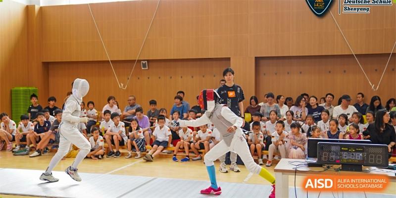 Two students are fencing on a court while other students watch from the side at HuZ Deutsche Schule Shenyang.