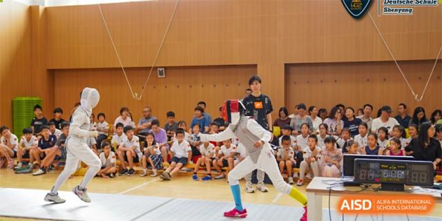 Two students are fencing on a court while other students watch from the side at HuZ Deutsche Schule Shenyang.