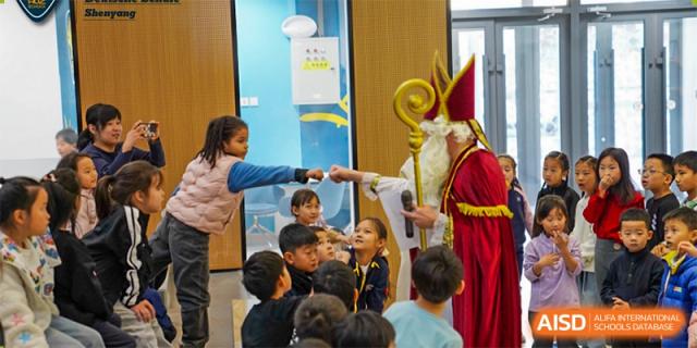 A group of young students is watching a man dressed as St. Nicholas at HuZ Deutsche Schule Shenyang.