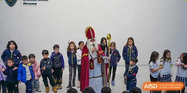 A man dressed as St. Nicholas is standing and speaking to a group of students at HuZ Deutsche Schule Shenyang.