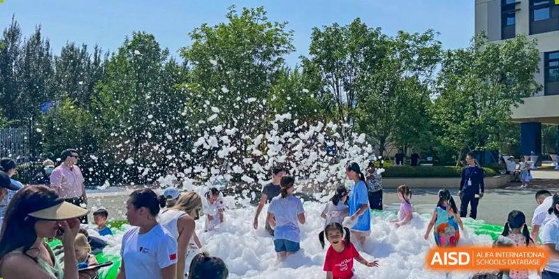 Students and children playing and laughing in a large pile of white foam at an outdoor event at HuZ Deutsche Schule Shenyang.