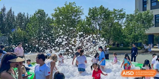 Students and children playing and laughing in a large pile of white foam at an outdoor event at HuZ Deutsche Schule Shenyang.