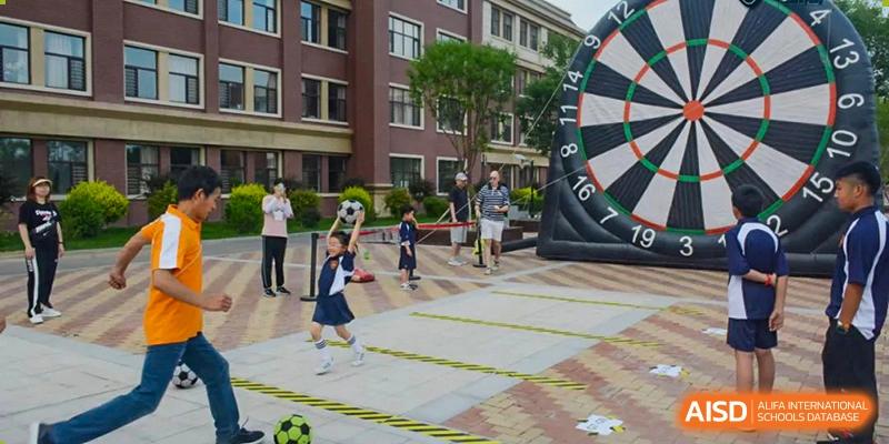 Students at HuZ Deutsche Schule Shenyang playing with a large dartboard and a soccer ball on a paved area.