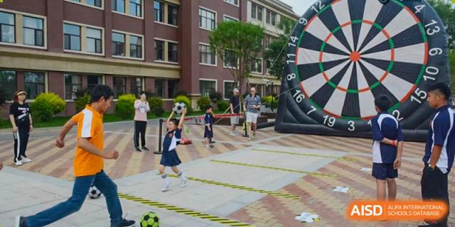 Students at HuZ Deutsche Schule Shenyang playing with a large dartboard and a soccer ball on a paved area.