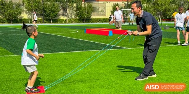 Students from HuZ Deutsche Schule Shenyang playing a game with red blocks on a green field.