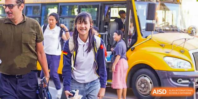 A smiling female student from HuZ Deutsche Schule Shenyang standing at the door of a school bus.