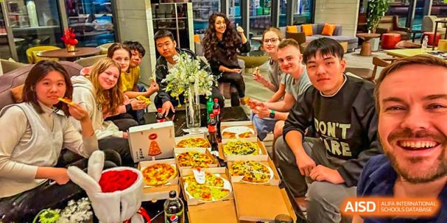 Students from HuZ Deutsche Schule Shenyang gathered around a table with pizzas during a school event.