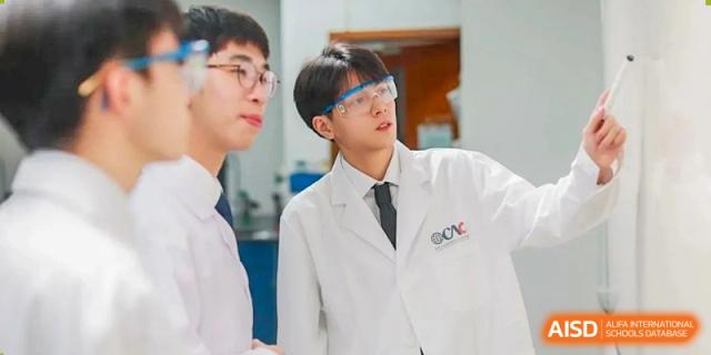 Two students from Overseas Chinese Academy of Chiway Suzhou in a science lab, one wearing a lab coat and goggles.