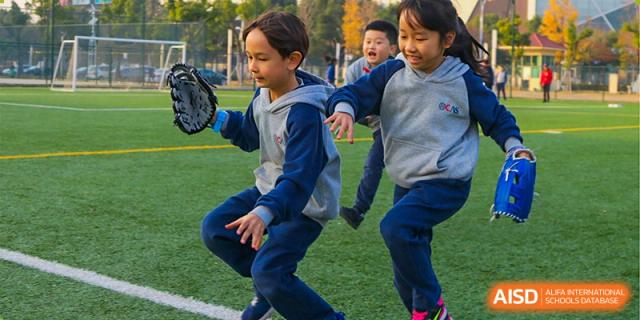 Two young students from Overseas Chinese Academy of Chiway Suzhou playing and running on a grassy field.