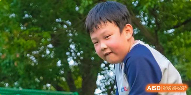 A close-up portrait of a young boy from Overseas Chinese Academy of Chiway Suzhou smiling outdoors.