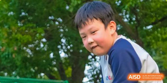 A close-up portrait of a young boy from Overseas Chinese Academy of Chiway Suzhou smiling outdoors.