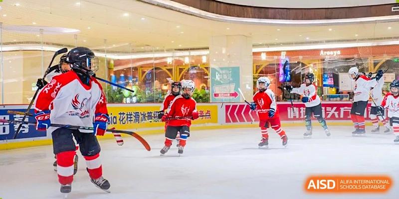 A group of students from Overseas Chinese Academy of Chiway Suzhou playing ice hockey indoors, wearing red uniforms and helmets.