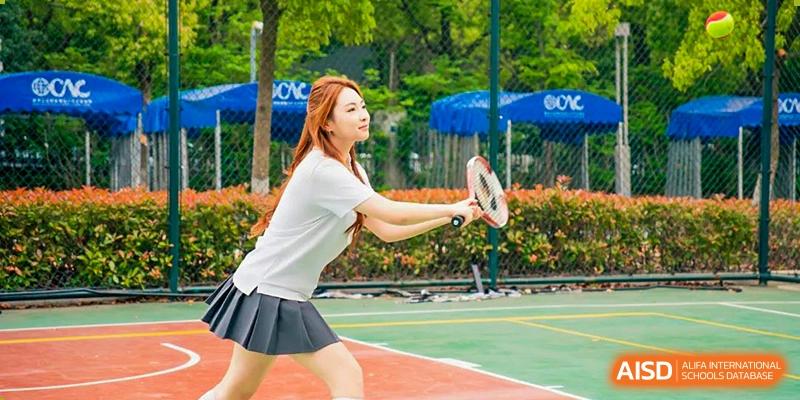 A female student from Overseas Chinese Academy of Chiway Suzhou playing tennis on an outdoor court.