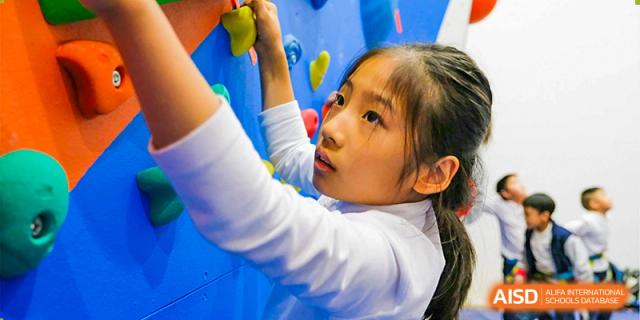 A young student from Overseas Chinese Academy of Chiway Suzhou climbing a colorful rock wall indoors.