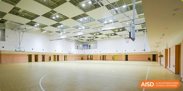 An empty, spacious indoor sports gymnasium at Overseas Chinese Academy of Chiway Suzhou with a wooden floor.