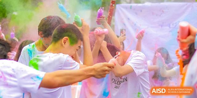Students from Overseas Chinese Academy of Chiway Suzhou participating in a color run or event, with colorful powder in the air.