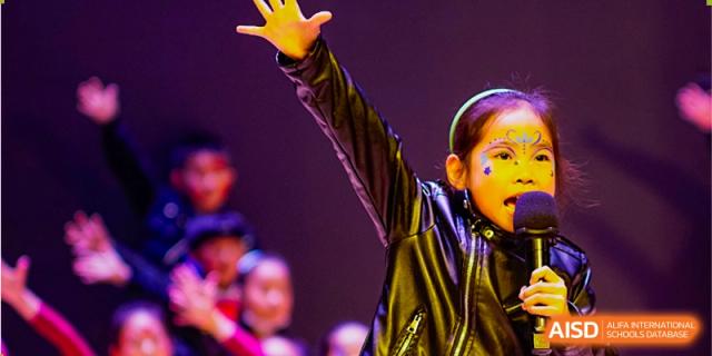 A close-up of a student from Overseas Chinese Academy of Chiway Suzhou raising their hand while performing on a stage.