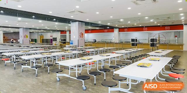 A spacious cafeteria at Overseas Chinese Academy of Chiway Suzhou with many white tables and chairs.