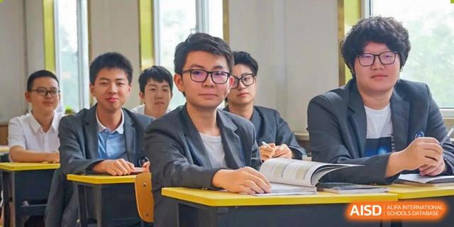 A male student wearing glasses and a blazer seated at a desk in a classroom at Shanxi Plinth International School.