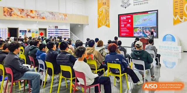 Students seated in yellow chairs facing a projector screen in a modern classroom or lecture hall at Shanxi Plinth International School.