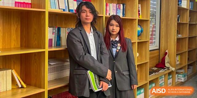 Two students, a male and a female, in matching gray blazers standing in front of a bookshelf at Shanxi Plinth International School.