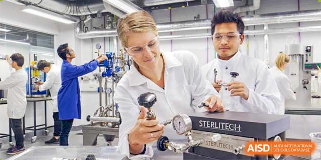 A scientist in goggles and a lab coat operates equipment next to a student in a laboratory at Shanxi Plinth International School.