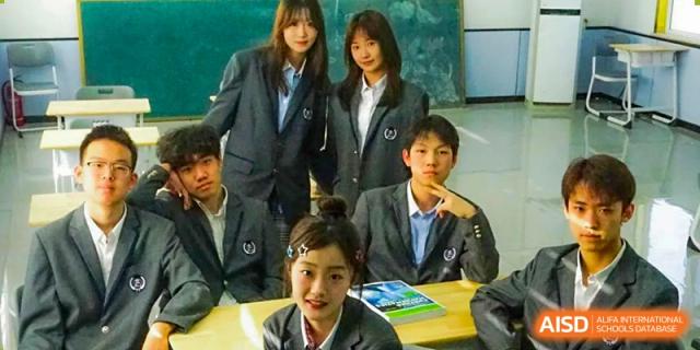 Group of smiling students in school uniforms sitting at a desk and posing for a photo at Shanxi Plinth International School.