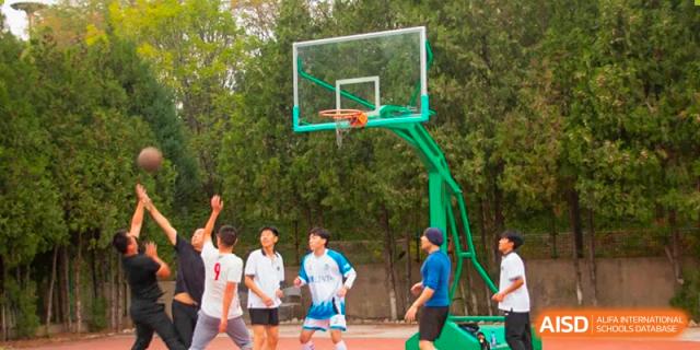 Students playing basketball on an outdoor court with a green hoop and backboard at Shanxi Plinth International School.